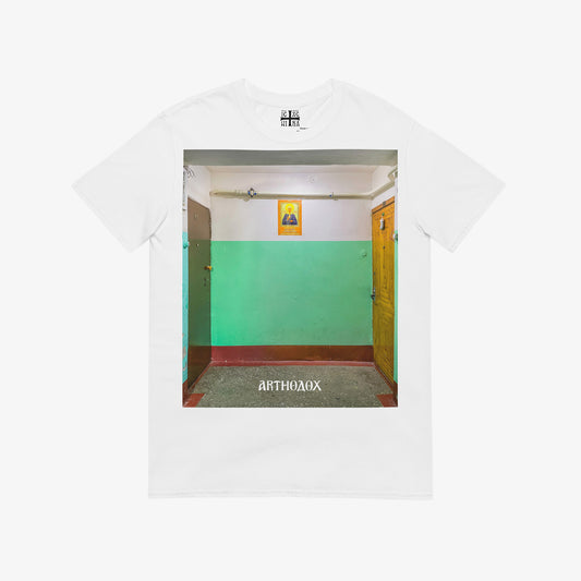 White unisex T-shirt with a large print depicting a typical Russian apartment stairwell featuring an icon of Holy Blessed Matrona of Moscow on the wall. From arthodox.com