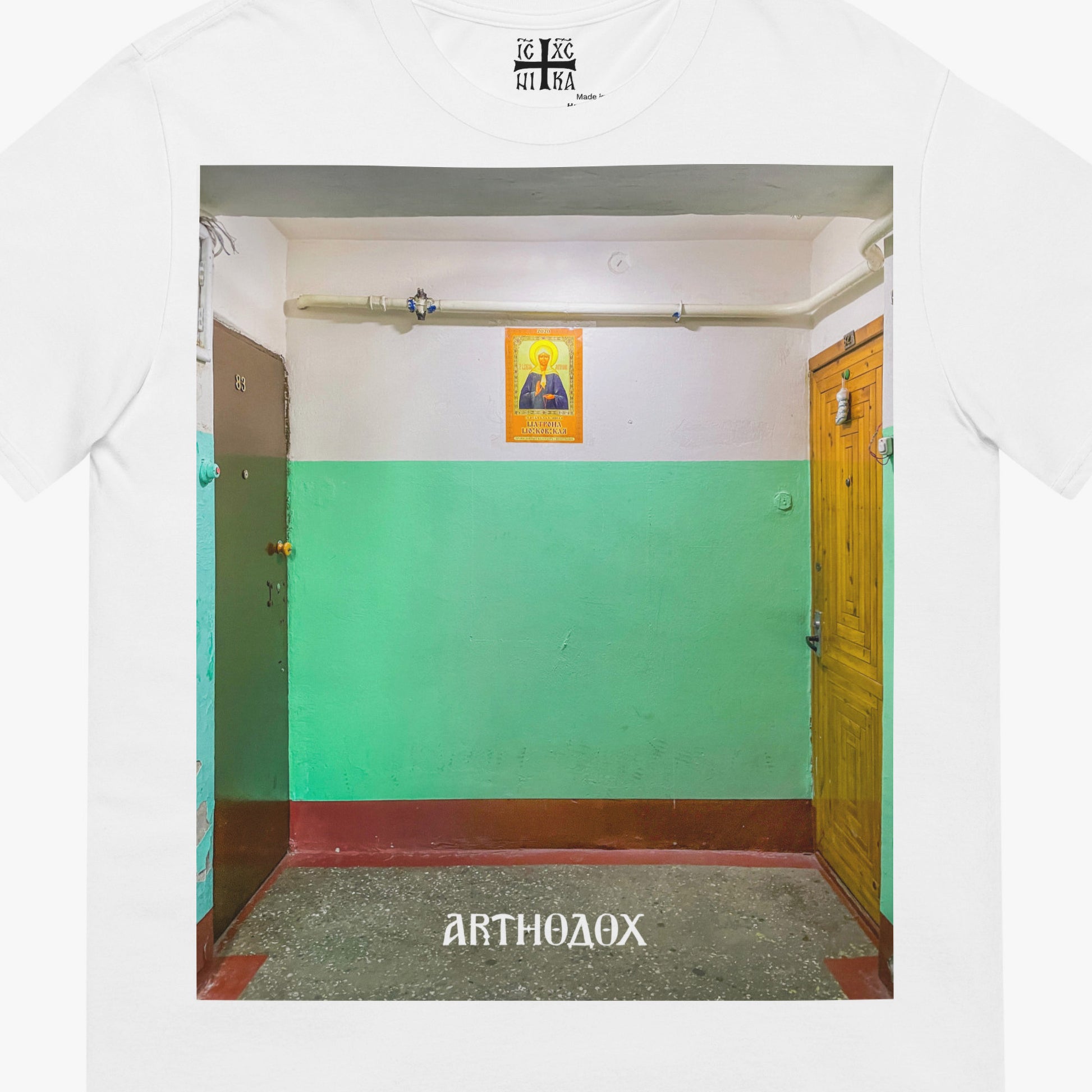 White unisex T-shirt with a large print depicting a typical Russian apartment stairwell featuring an icon of Holy Blessed Matrona of Moscow on the wall. Closeup photo. From arthodox.com